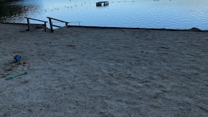 Une plage de sable avec une jetée en bois et une vue dégagée sur un lac entouré de collines.