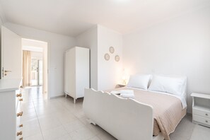 A bedroom with a bed, bedside tables, a wardrobe, and a door leading to another room.