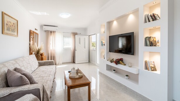 A modern living room with a sofa, a coffee table, a TV mounted on the wall, and built-in shelves with books and decorative items.