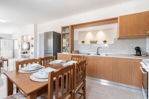 A modern kitchen with wooden cabinets, a built-in oven, and a dining area with a wooden table and chairs.