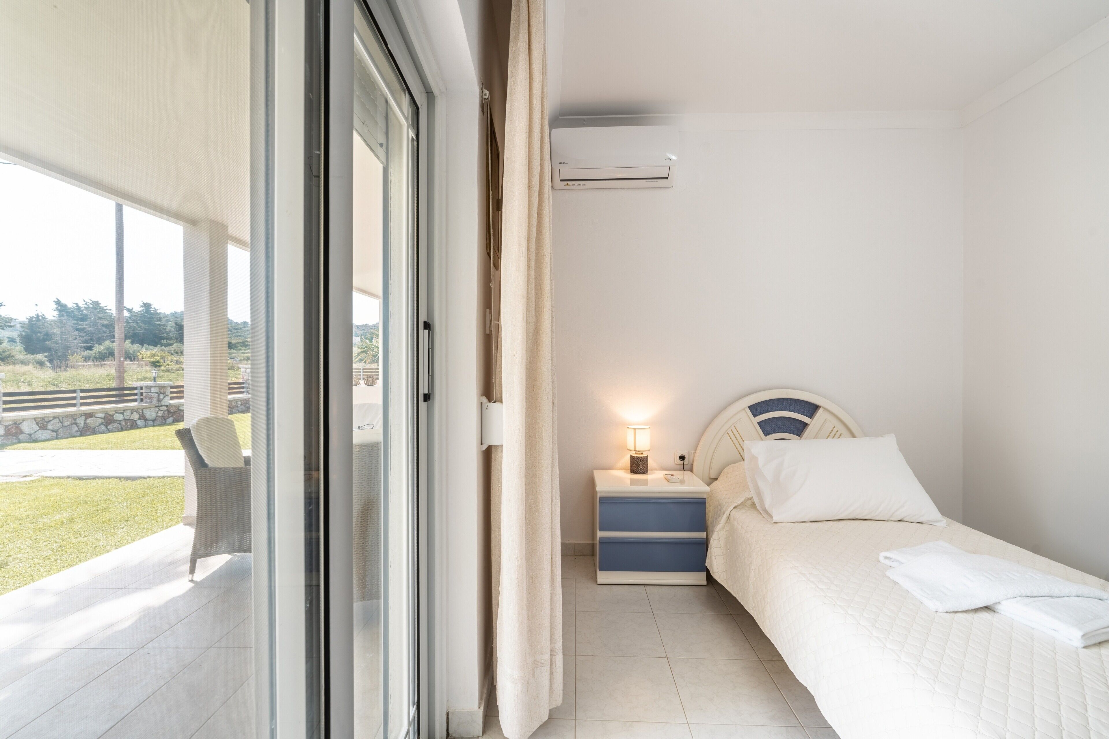 Een slaapkamer met een bed, nachtkastje en een raam met uitzicht op de omgeving.