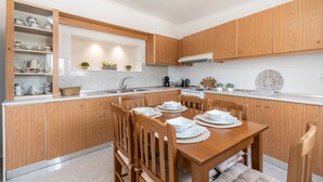 A modern kitchen with wooden cabinets, a dining table set for four, and a built-in shelf with kitchenware.