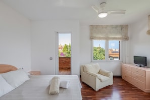 Une chambre à coucher comprenant un lit, une télévision, un canapé et une fenêtre donnant sur des immeubles et des arbres.