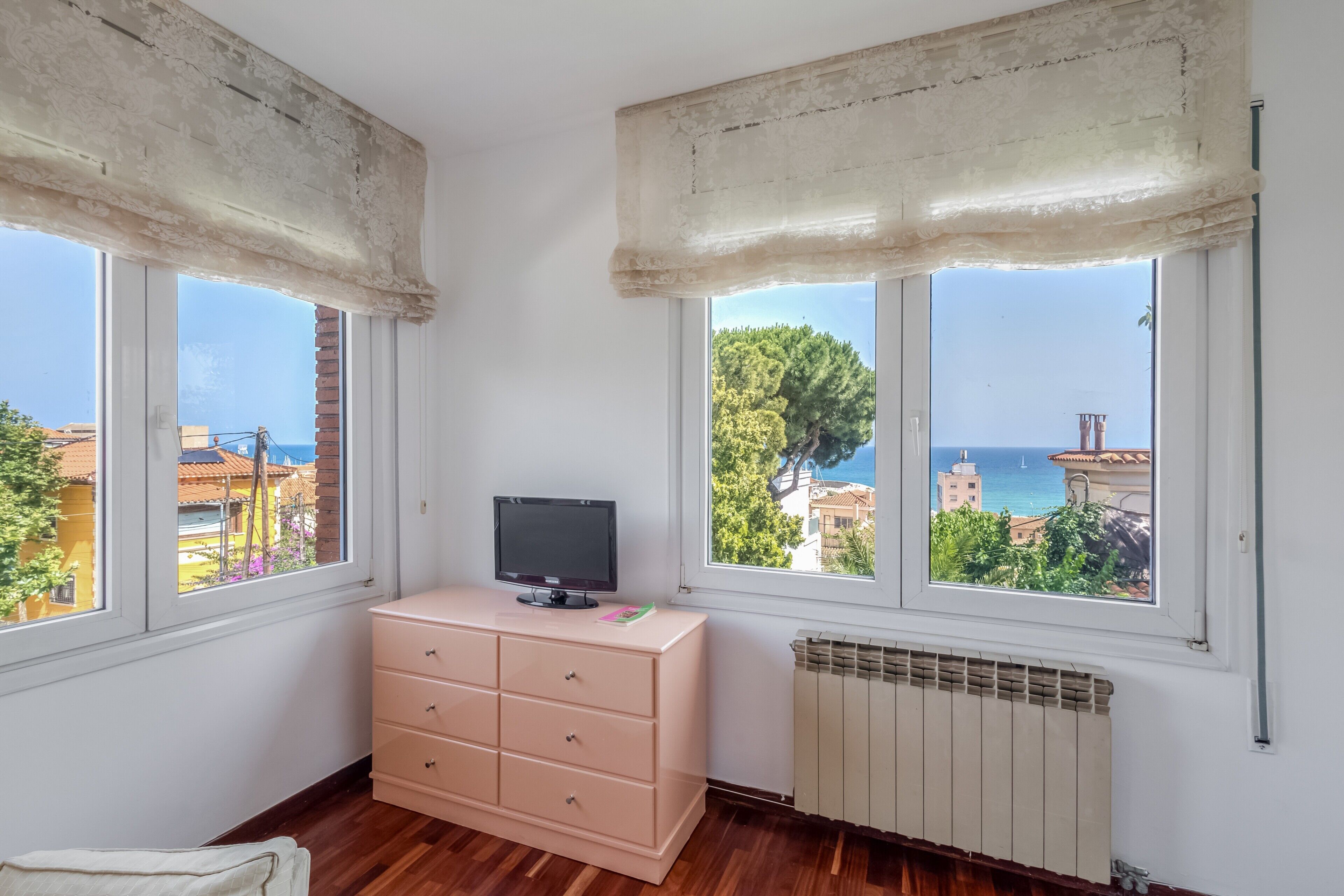 A room with two windows, a radiator, and a pink dresser with a television.