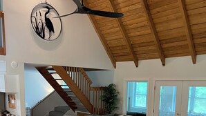 Ampla sala de estar com sofá modular cinza, escada de madeira e ventilador de teto.