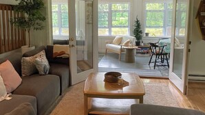 Un salon spacieux doté d’un plafond en bois, d’une grande fenêtre et d’une porte-fenêtre coulissante donnant sur un espace extérieur.