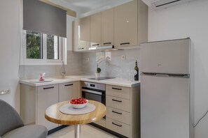 A modern kitchen with beige cabinets, a white refrigerator, and a round wooden table with a bowl of fruit.