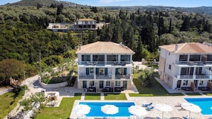 Un edificio su due piani con piscina, immerso nel verde e circondato da colline.