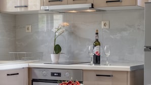 Una cucina moderna con schienale in marmo, un'orchidea in vaso, una bottiglia di vino e una ciotola di ciliegie sul piano di lavoro.