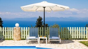 Zona piscina con due lettini, un ombrellone e un pilastro in pietra.
