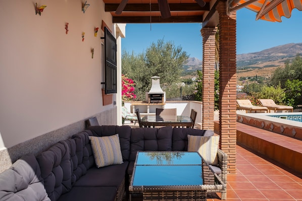 Un área de estar al aire libre techada con sofá, mesa y parrilla.