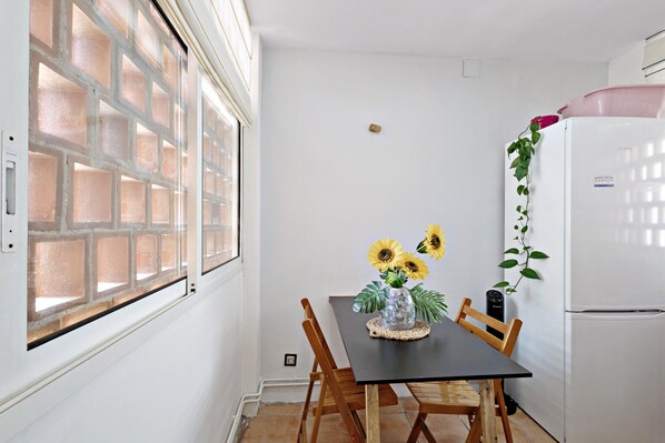 A kitchen with a table, chairs, a refrigerator, and a window with a brick pattern.