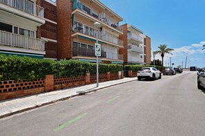 Un immeuble résidentiel à plusieurs étages, doté de balcons et d’une façade en briques, se dressant sous un ciel d’un bleu limpide.