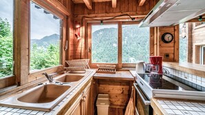 A wooden cabin kitchen with two sinks, a stove, and a window overlooking a forested mountain.