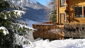 A wooden cabin with a balcony, surrounded by snow-covered trees and mountains.