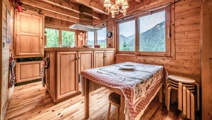 A wooden cabin interior with a kitchen, dining table, and a view of mountains.