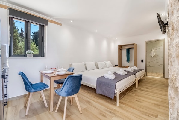 A modern bedroom with a bed, a desk, two chairs, a window, and a shower area.