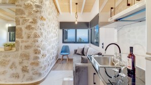 A modern kitchen with a stone wall, a blue chair, a sofa, and a wine bottle. - Studio Apartment '3' with Sea View, Wi-Fi and Air Conditioning (?e???da)