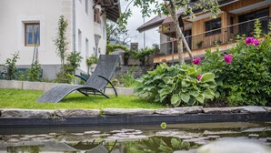 A garden with a pond, a chair, and a building with balconies. - Residence Grünbacher Apartment 4 with Balcony and Shared Pool (Issengo)
