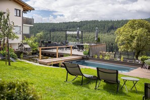 A backyard with a swimming pool, outdoor furniture, and a view of a forested hill. - Residence Grünbacher Apartment 5 (Issengo)