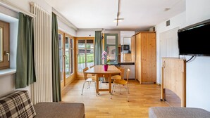 Een moderne woonkamer met een houten eettafel, twee banken, een televisie en een keukenhoek.