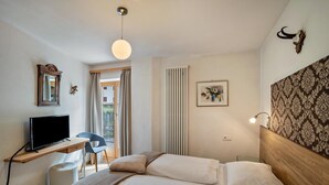 Un dormitorio con cama, escritorio con televisor, silla, ventana y lámpara de pared.