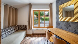 Una habitación con sofá, mesa de comedor, ventana con cortinas, radiador y espejo adosado a la pared.