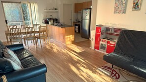 Ein modernes Wohnzimmer mit einer Couch, einem Essbereich mit Stühlen, einer Küche mit Kühlschrank und Herd sowie Kunstwerken an den Wänden.