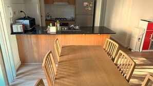 Eine moderne Küche mit Holzausstattung, einem Edelstahlkühlschrank, einem eingebauten Gasherd und einem Essbereich mit Holztisch und Stühlen.