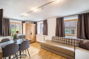 Une pièce comprenant une table à manger, des chaises, un canapé, un meuble et une fenêtre avec des rideaux.
