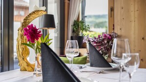 Una mesa de comedor dispuesta con platos, cubiertos y vasos, un mantel individual negro, un adorno dorado y un florero con flores.