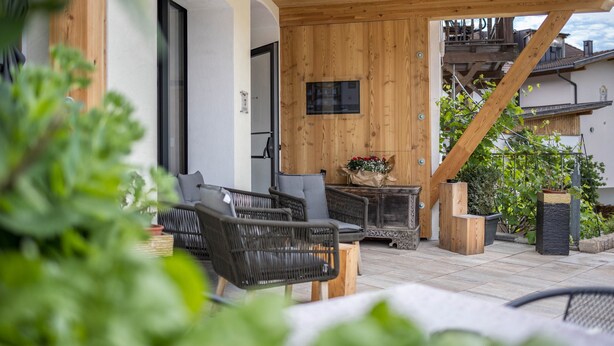 Un patio al aire libre con mobiliario de mimbre, una terraza de madera y plantas en macetas.