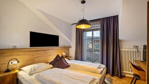 A hotel room with a bed, a desk, a chair, a TV, and a window with curtains. - Residence Grünbacher Apartment 2 with Balcony and Shared Pool (Issengo)