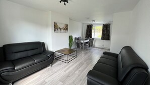 Un salon moderne avec deux canapés en cuir noir, une table basse en verre et un coin repas comprenant une table et des chaises blanches.