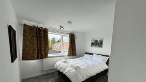 Une chambre avec un lit simple, un radiateur, une fenêtre avec des rideaux, un tableau au mur et une petite table.