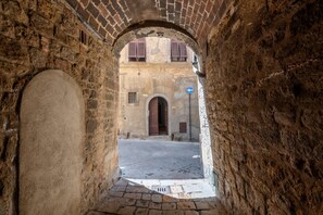 An arched stone passageway leading to a building with a visible door and a blue directional sign.