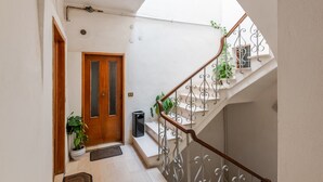 A narrow hallway with a wooden door, a staircase with metal railings, and potted plants. - Apartment 'Appartamento Nel Cuore Di Volterra' (Volterra)
