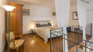 Ein Schlafzimmer mit einem Bett, einem Sessel, einem Nachttisch, einer Lampe und einem Balkon mit Geländer.
