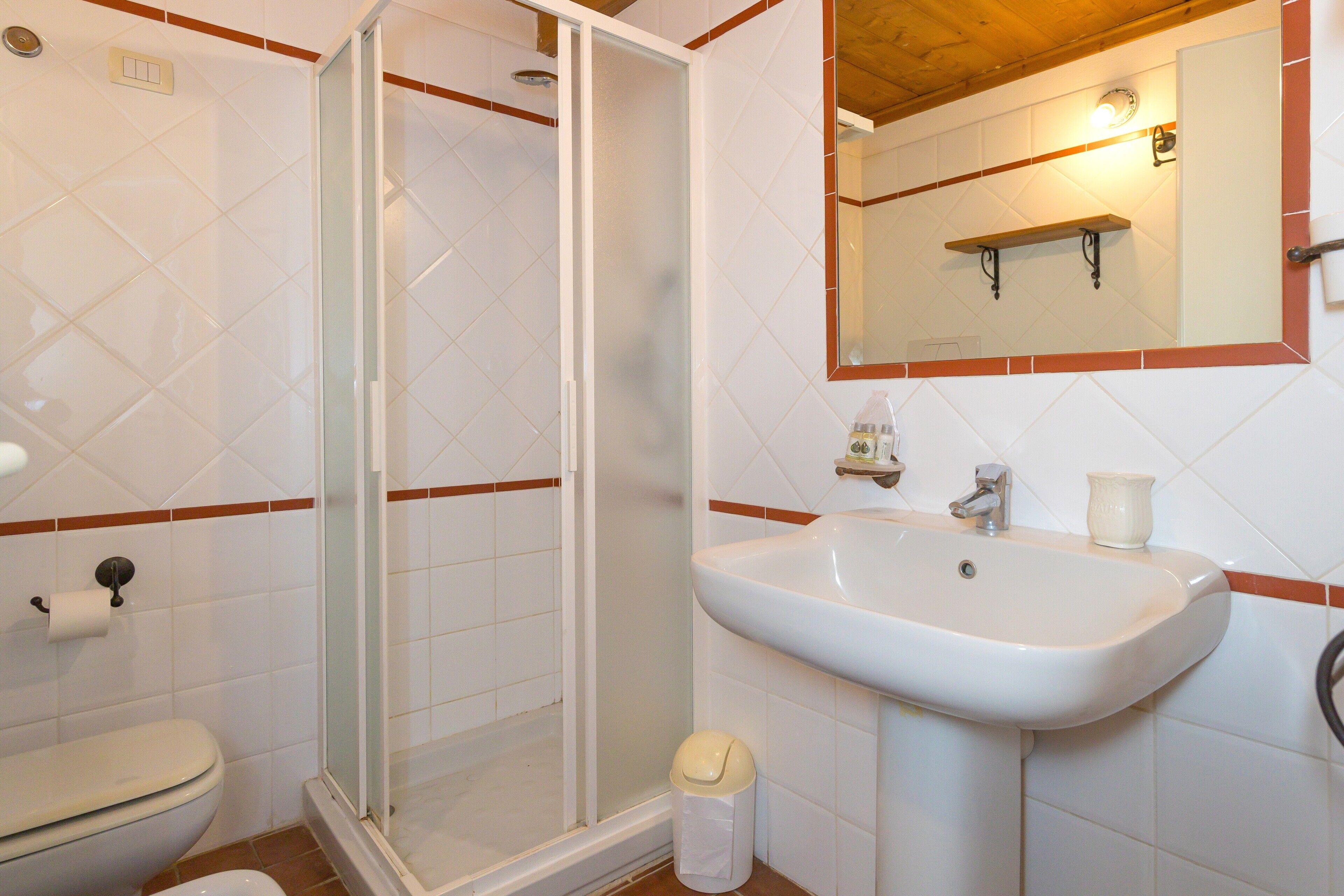 Un baño con inodoro, lavamanos, cabina de ducha de vidrio y espejo.