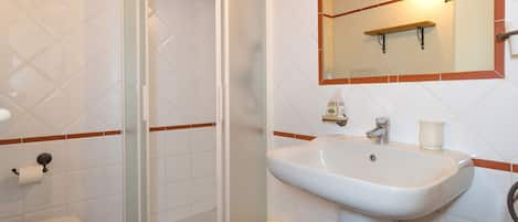 Un baño con inodoro, lavamanos, cabina de ducha de vidrio y espejo.