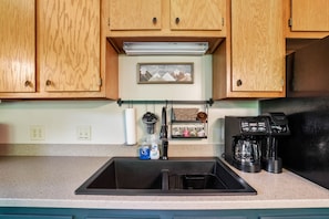 A kitchen with wooden cabinets, a stainless steel sink, a coffee maker, and a hanging rack with kitchen utensils.