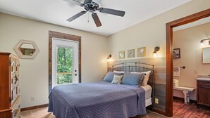 Ein Schlafzimmer mit einem Bett, einem Deckenventilator, einer Tür zu einem Balkon und einem kleinen Badezimmer.