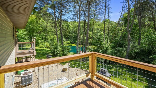 Eine Holzterrasse mit Metallgeländer, die einen üppigen grünen Landschaftsbereich und einen Teich überblickt.