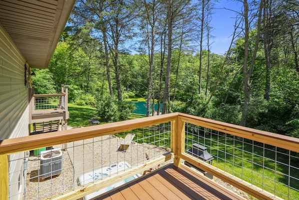 A wooden deck with a metal railing overlooking a lush green landscape and a pond.