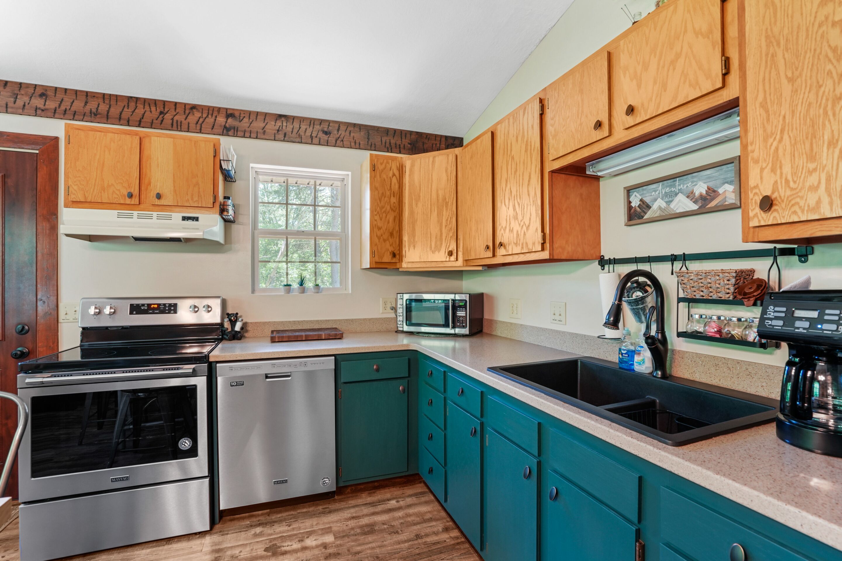 A modern kitchen with wooden cabinets, stainless steel appliances, and teal countertops.