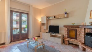 A living room with a TV, fireplace, bookshelf, and a view of balconies through a door.