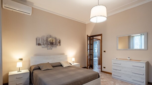 A bedroom with a bed, bedside tables, a dresser, a mirror, and a ceiling light.