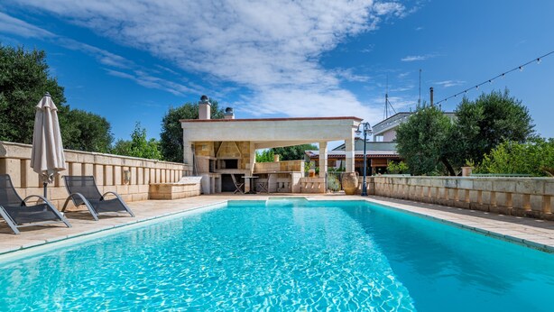 A swimming pool with lounge chairs, a covered patio, and a stone wall. - Villa 'Casa Rocco, Private Pool' with Private Pool, Wi-Fi and Air Conditioning (Ceglie Messapica)