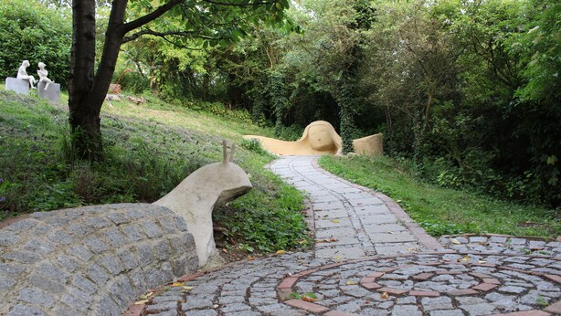 Un sendero de piedra que atraviesa un parque con esculturas y follaje.