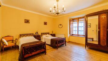 A bedroom with two wooden beds, a wooden wardrobe, a window with curtains, and a chandelier.